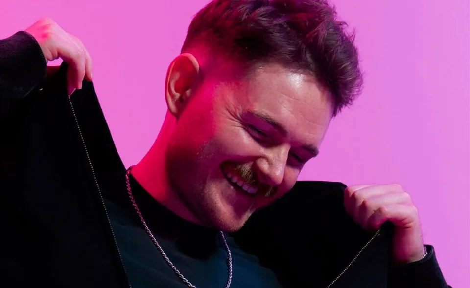 AVELLO smiling in a black jacket under pink studio lighting.