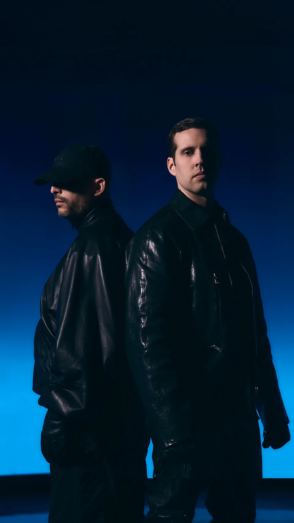 SLANDER’s two members in dark jackets against a blue-lit background.